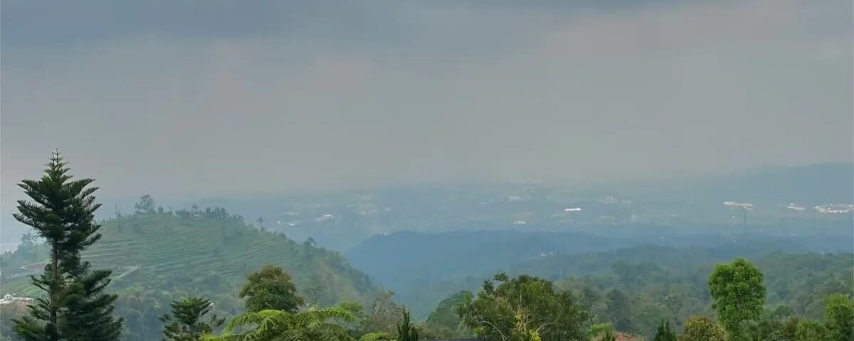 Circular infinity pool on a hillside resort, people lounging and swimming with a green valley and cloudy sky in the distance