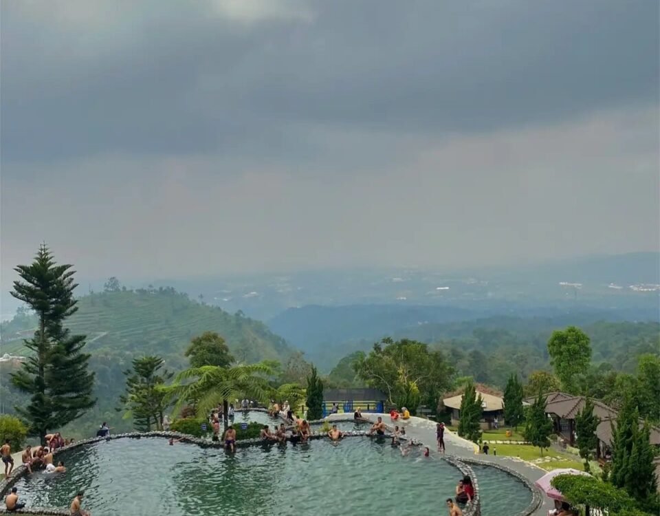 Circular infinity pool on a hillside resort, people lounging and swimming with a green valley and cloudy sky in the distance