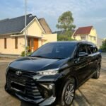 snaptik_7369070534291623174_2_v2 - Dyantransport Black Toyota SUV parked in a suburban driveway with beige houses and a tree in the background, under a blue sky.
