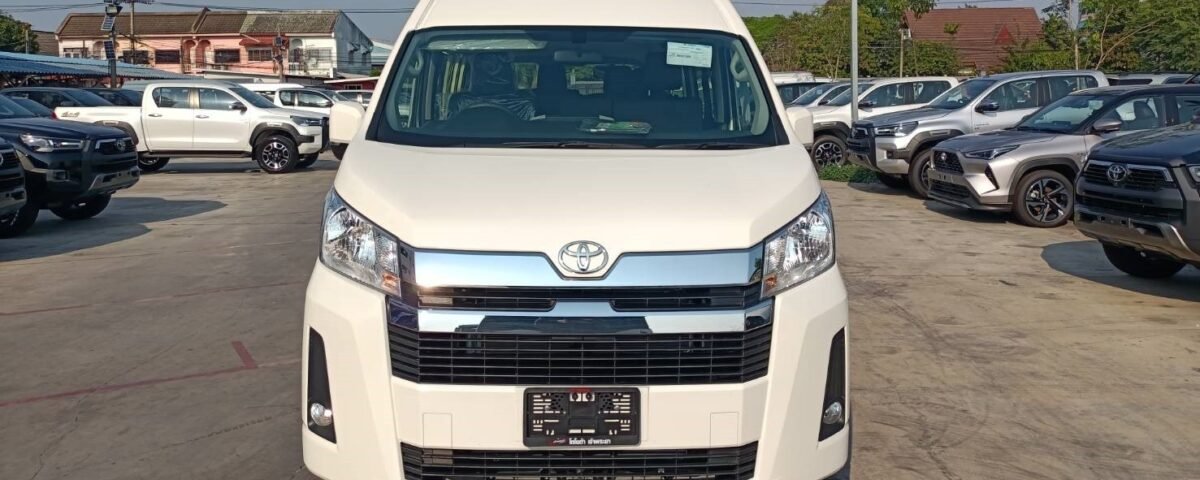Front view of a white Toyota minivan parked in a car dealership lot with other vehicles in the background.
