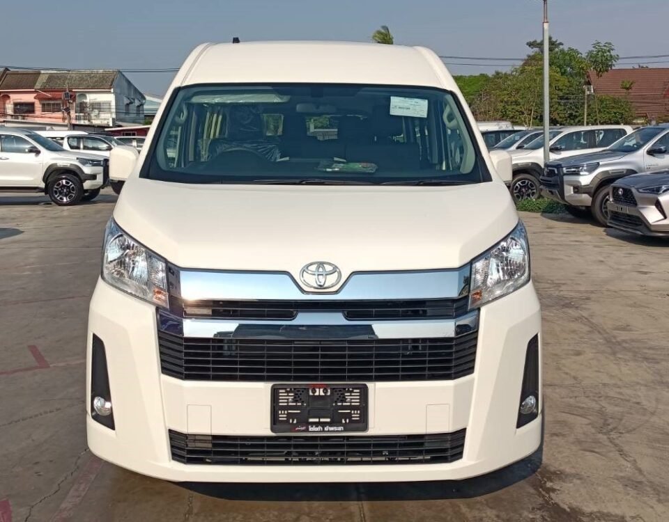 Front view of a white Toyota minivan parked in a car dealership lot with other vehicles in the background.