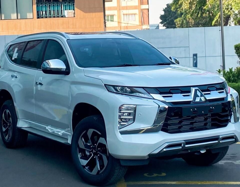 White Mitsubishi SUV parked diagonally in a bright parking lot near a shopping center, with a pink Solaria sign in the background and blue sky above.