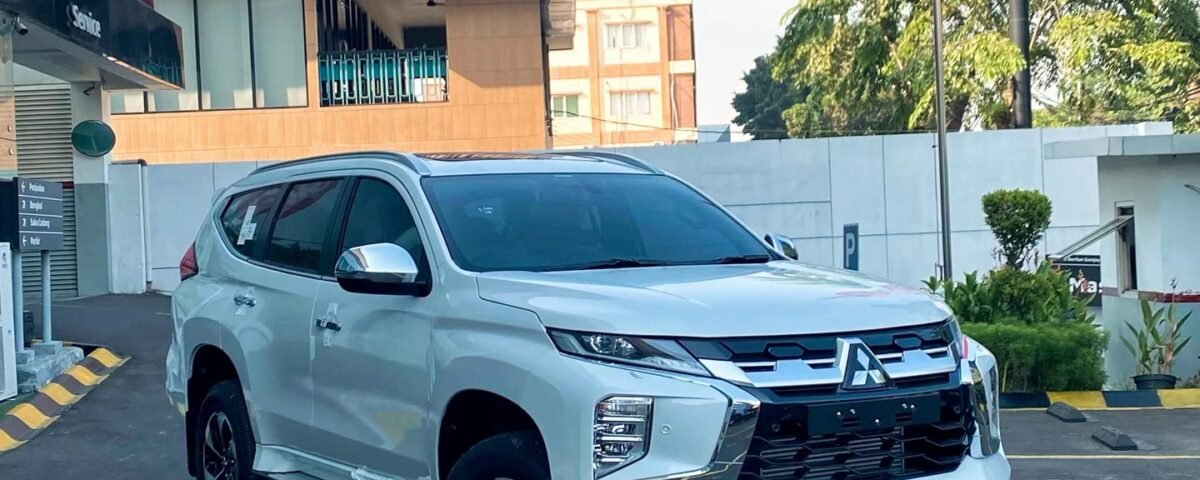 White Mitsubishi SUV parked diagonally in a parking lot near a storefront and a pink Solaria sign in the background.