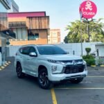 White Mitsubishi SUV parked diagonally in a parking lot near a storefront and a pink Solaria sign in the background.