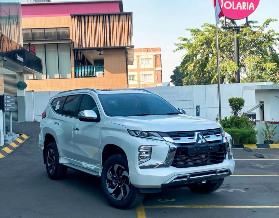 White Mitsubishi SUV parked diagonally in a parking lot near a storefront and a pink Solaria sign in the background.