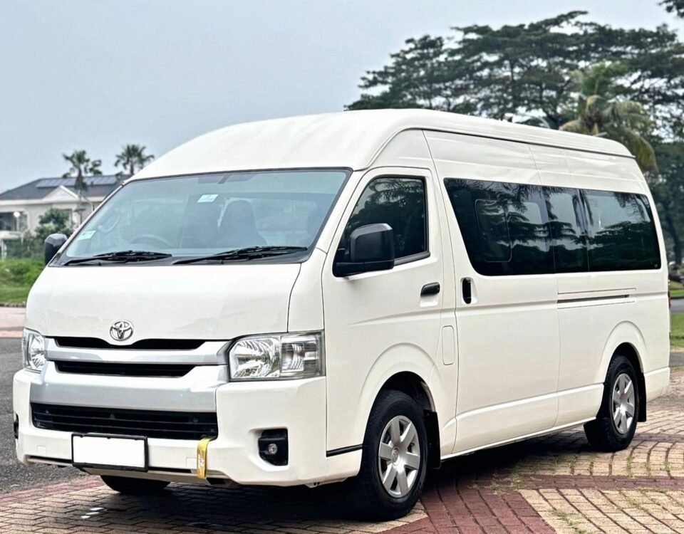 White Toyota van with a high roof parked on a brick-paved lot, with trees in the background.