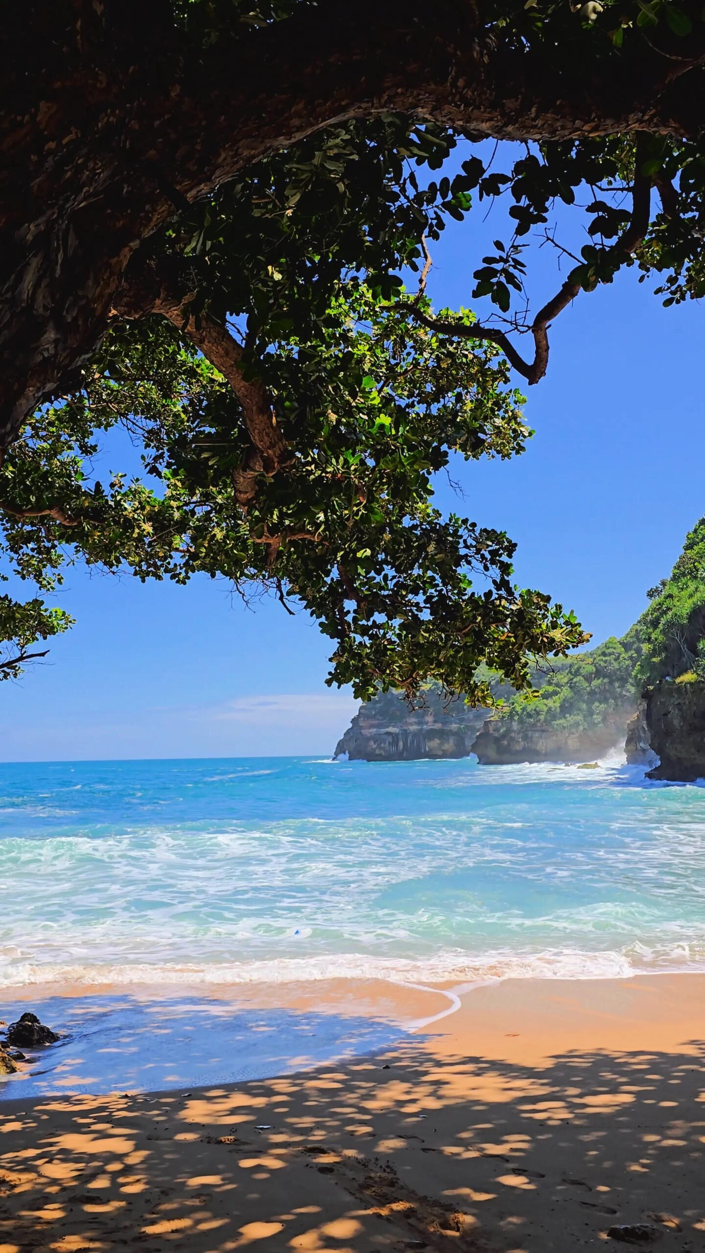 Pantai dengan pulau karang kecil di tengah yang membagi area ombak tenang dan ombak besar.