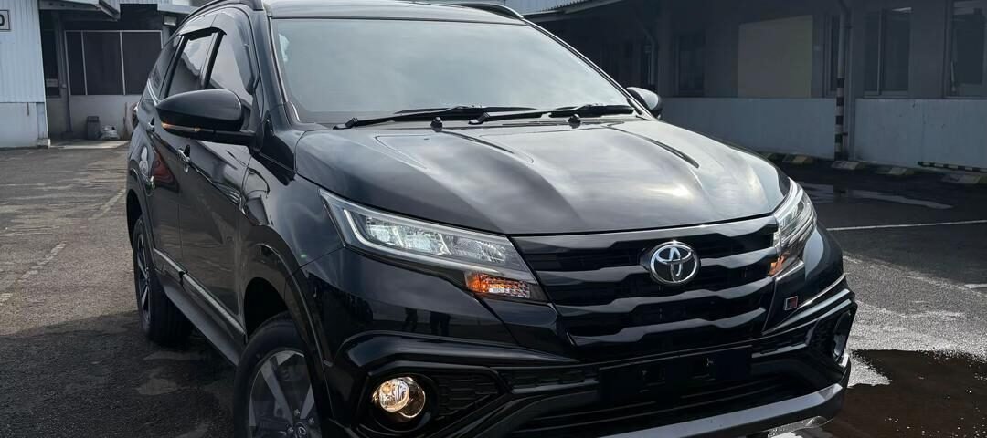 Black Toyota SUV parked in an industrial parking lot, seen from the front three-quarter angle with a tall metal watchtower in the background.