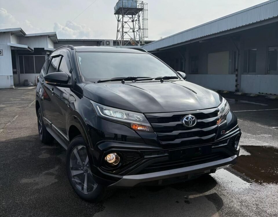 Black Toyota SUV parked in an industrial parking lot, seen from the front three-quarter angle with a tall metal watchtower in the background.