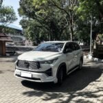 snaptik_7540270045507669265_1_v2 - Dyantransport White SUV parked on a brick-paved area with trees and a building in the background (front three-quarter view).