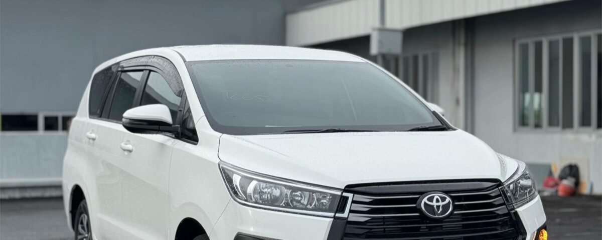 Front three-quarter view of a white Toyota SUV parked in a paved lot, with industrial buildings in the background.