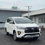 Front three-quarter view of a white Toyota SUV parked in a paved lot, with industrial buildings in the background.