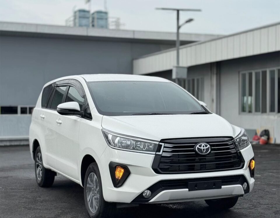 Front three-quarter view of a white Toyota SUV parked in a paved lot, with industrial buildings in the background.