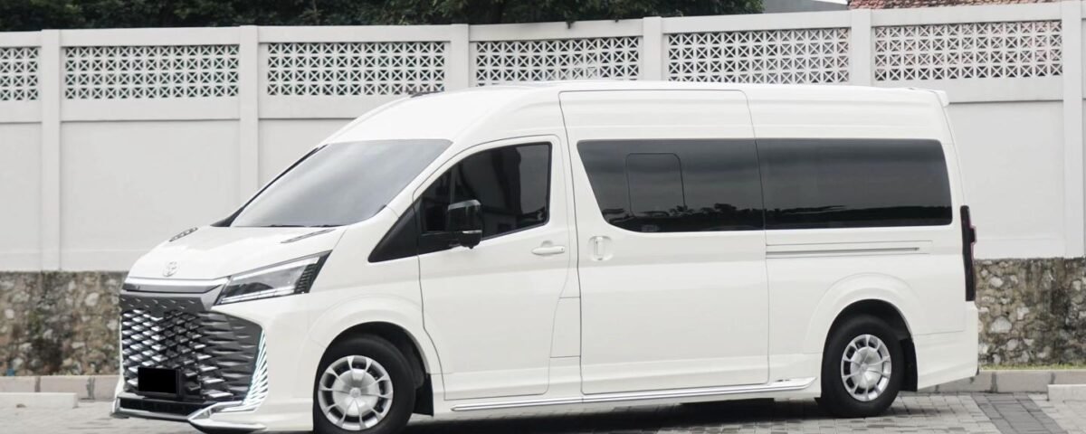 White modern white van parked on a brick-paved lot in front of a white lattice fence with green trees in the background.