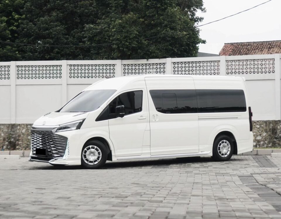 White modern white van parked on a brick-paved lot in front of a white lattice fence with green trees in the background.