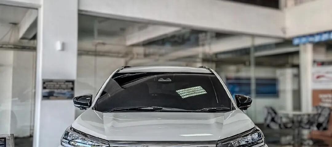 snaptik_7616595255483272469_1_v2 - Dyantransport Front view of a white Toyota Veloz Hybrid EV on a showroom floor with a bold black grille.
