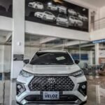 snaptik_7616595255483272469_1_v2 - Dyantransport Front view of a white Toyota Veloz Hybrid EV on a showroom floor with a bold black grille.