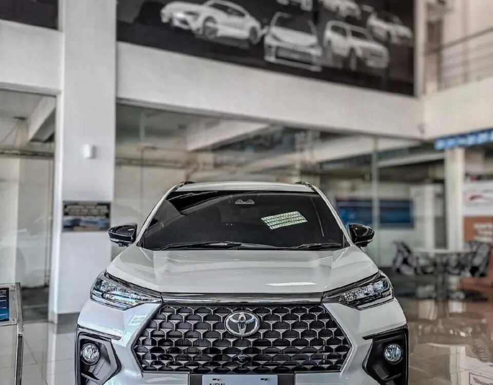 snaptik_7616595255483272469_1_v2 - Dyantransport Front view of a white Toyota Veloz Hybrid EV on a showroom floor with a bold black grille.