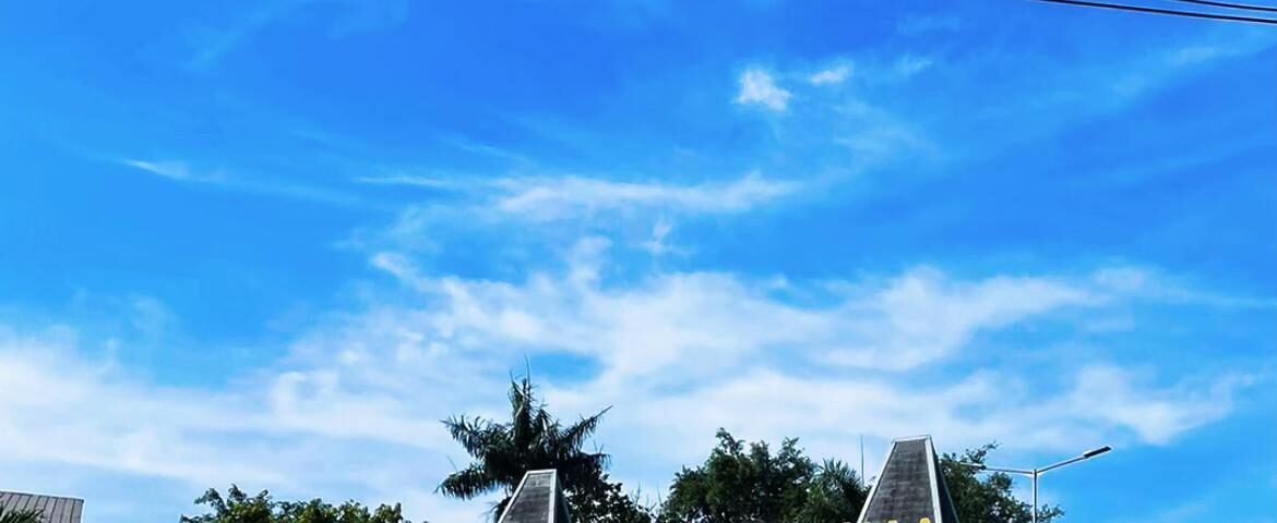 Entrance sign for Halim Perdanakusuma Airport against a bright blue sky with power lines overhead and a circular driveway in the foreground.