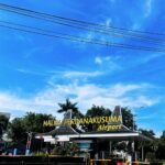 Entrance sign for Halim Perdanakusuma Airport against a bright blue sky with power lines overhead and a circular driveway in the foreground.