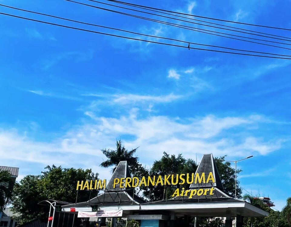 Entrance sign for Halim Perdanakusuma Airport against a bright blue sky with power lines overhead and a circular driveway in the foreground.