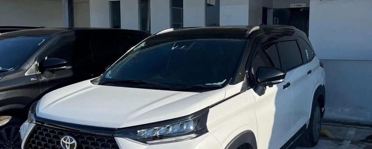 White Toyota SUV parked under a concrete canopy beside a building with a Musholla sign on the wall.