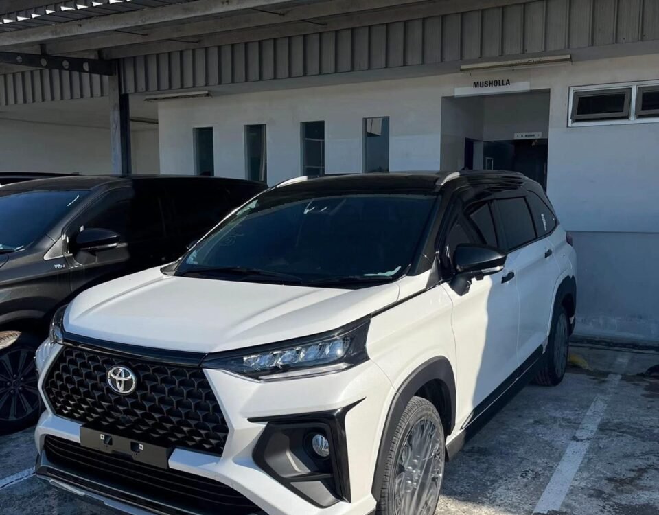 White Toyota SUV parked under a concrete canopy beside a building with a Musholla sign on the wall.