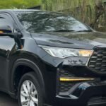 Black Toyota SUV parked on a street beside a tree and a modern gray building.
