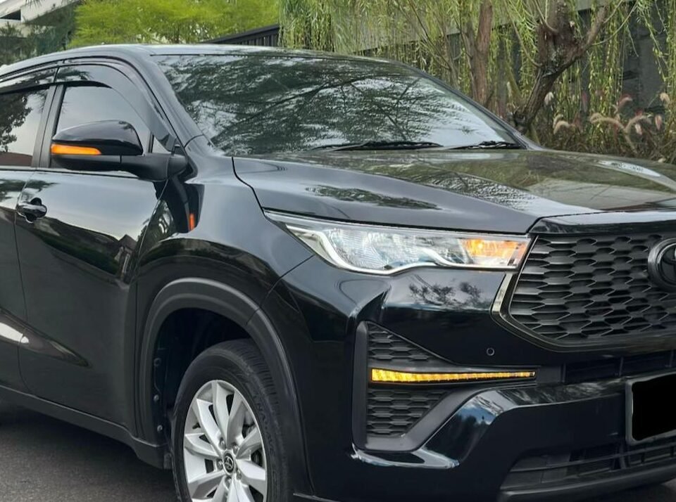 Black Toyota SUV parked on a street beside a tree and a modern gray building.