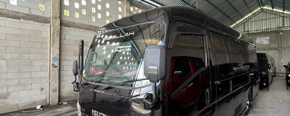 Black Isuzu passenger van parked inside a large industrial warehouse with a corrugated metal roof and blue steel beams