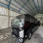 Black Isuzu passenger van parked inside a large industrial warehouse with a corrugated metal roof and blue steel beams