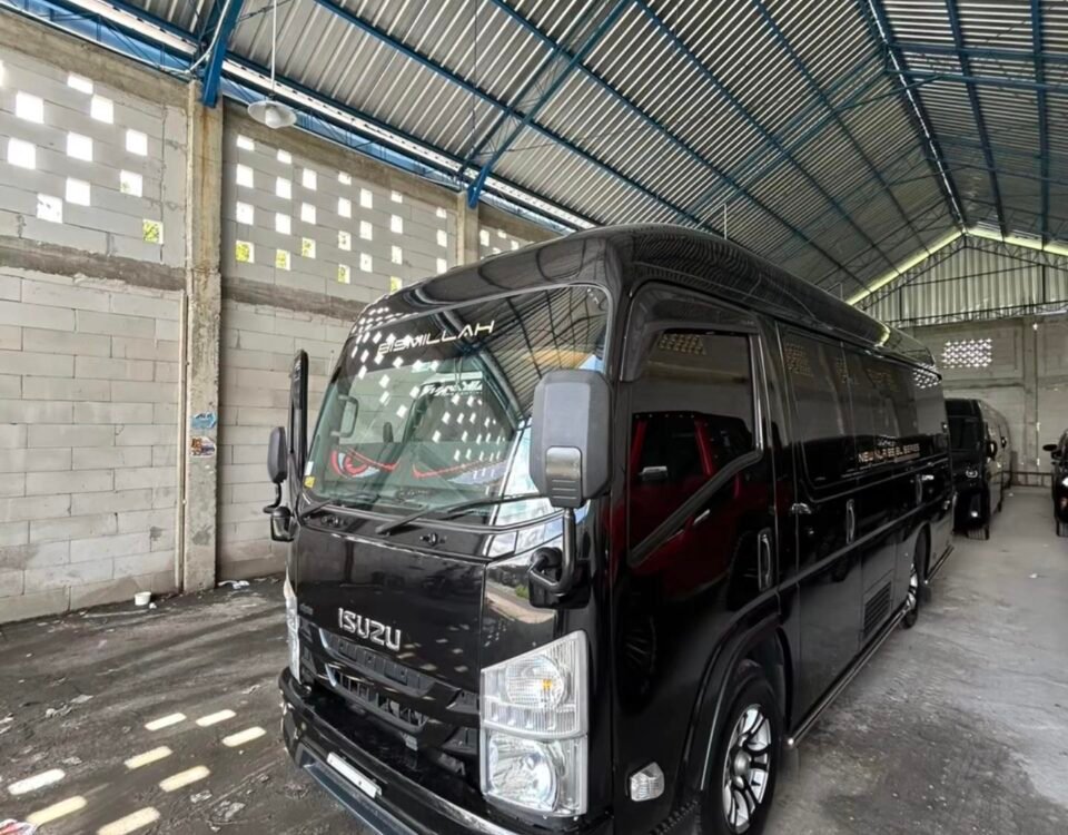 Black Isuzu passenger van parked inside a large industrial warehouse with a corrugated metal roof and blue steel beams