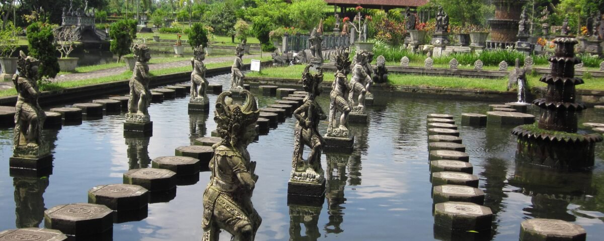 Stone statues rising from a reflective pond, lined by square stepping stones in a lush temple garden.