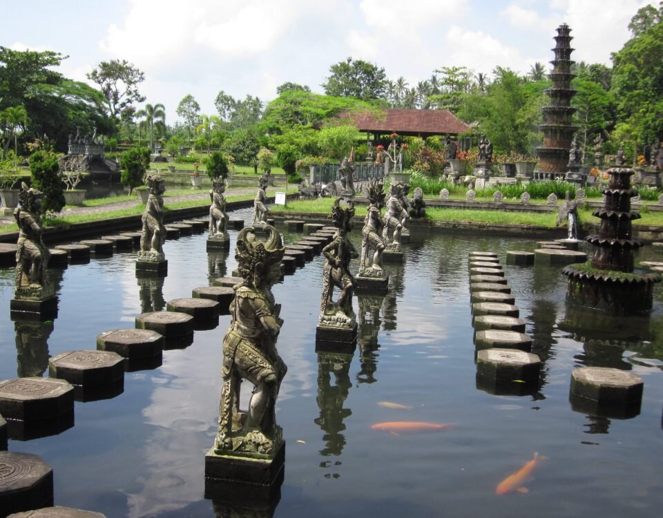 Stone statues rising from a reflective pond, lined by square stepping stones in a lush temple garden.