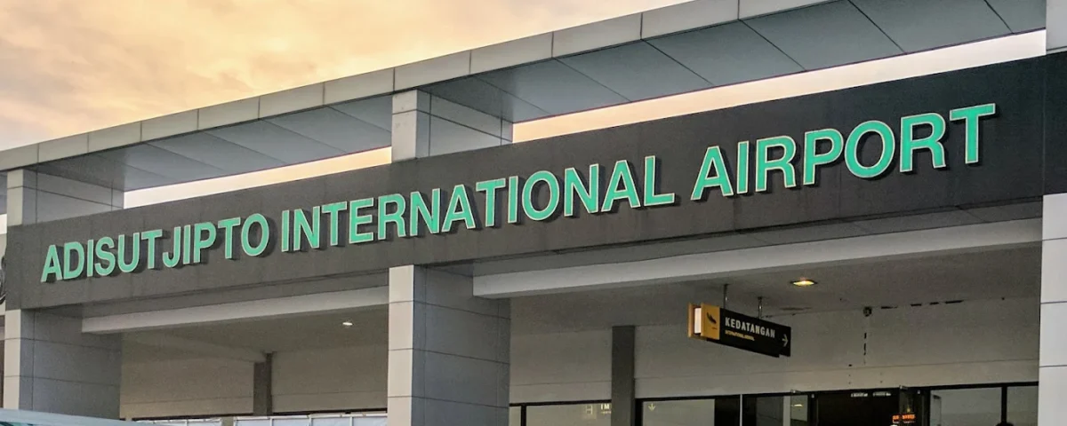 Facade of Adisutjipto International Airport with green lettering and a visible arrivals sign above the entrance.