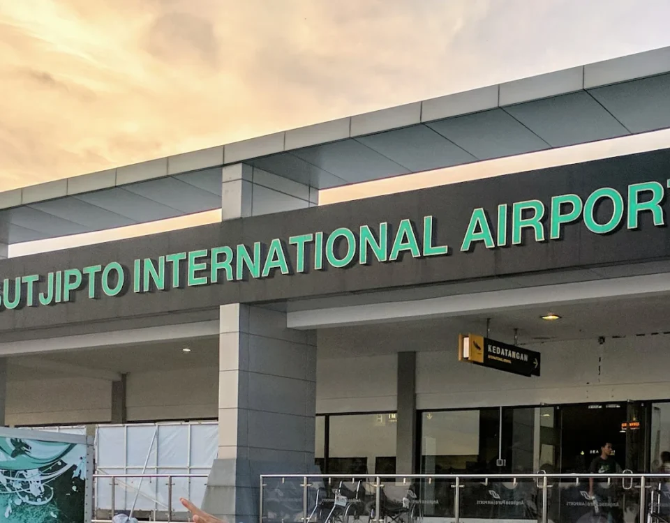 Facade of Adisutjipto International Airport with green lettering and a visible arrivals sign above the entrance.
