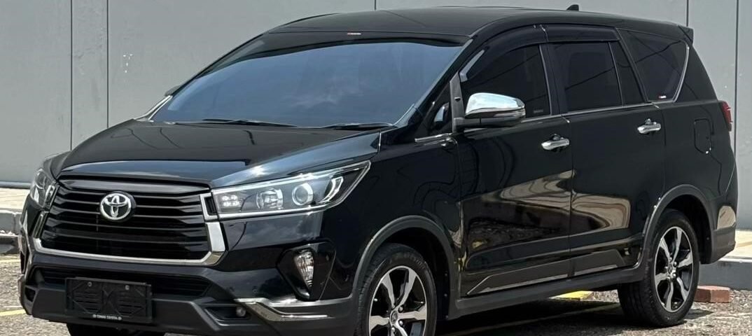 Black Toyota SUV (Highlander) in a parking lot near a grey panel wall, seen from a front-three-quarter angle with tinted windows.