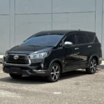 Black Toyota SUV (Highlander) in a parking lot near a grey panel wall, seen from a front-three-quarter angle with tinted windows.