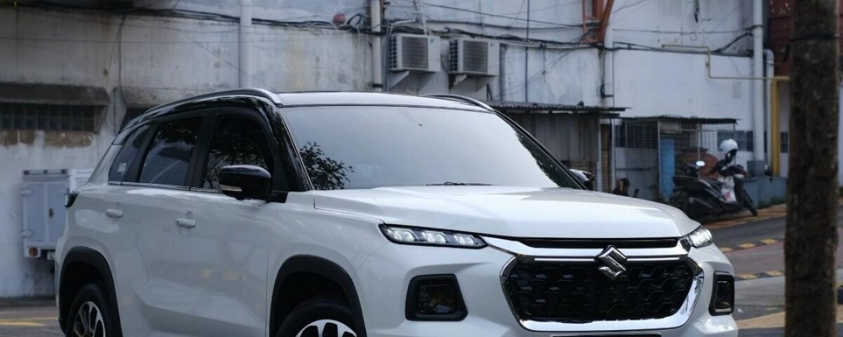 White SUV parked on a city street with a building and orange water tanks on a raised platform in the background.