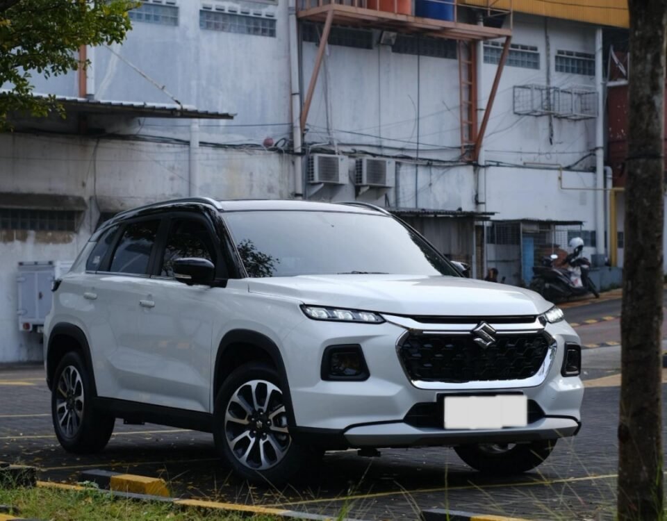 White SUV parked on a city street with a building and orange water tanks on a raised platform in the background.