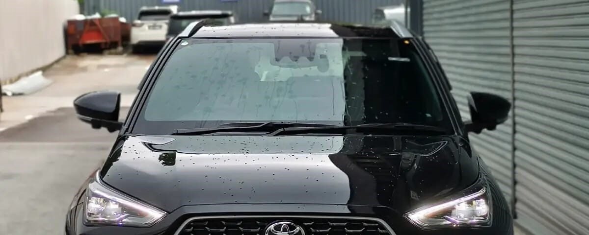 Front view of a black Toyota SUV parked in a narrow lot, raindrops on the hood and windshield, with a metal shutter on the right.