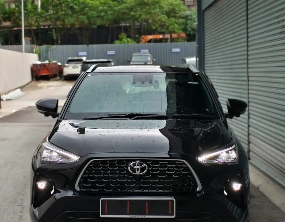 Front view of a black Toyota SUV parked in a narrow lot, raindrops on the hood and windshield, with a metal shutter on the right.