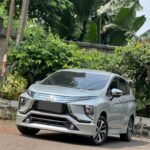 Silver Mitsubishi SUV parked on a street beside lush green tropical plants and a concrete wall.