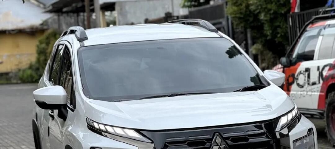 Front three-quarter view of a white Mitsubishi SUV parked on a brick-paved street in a residential area with houses in the background.