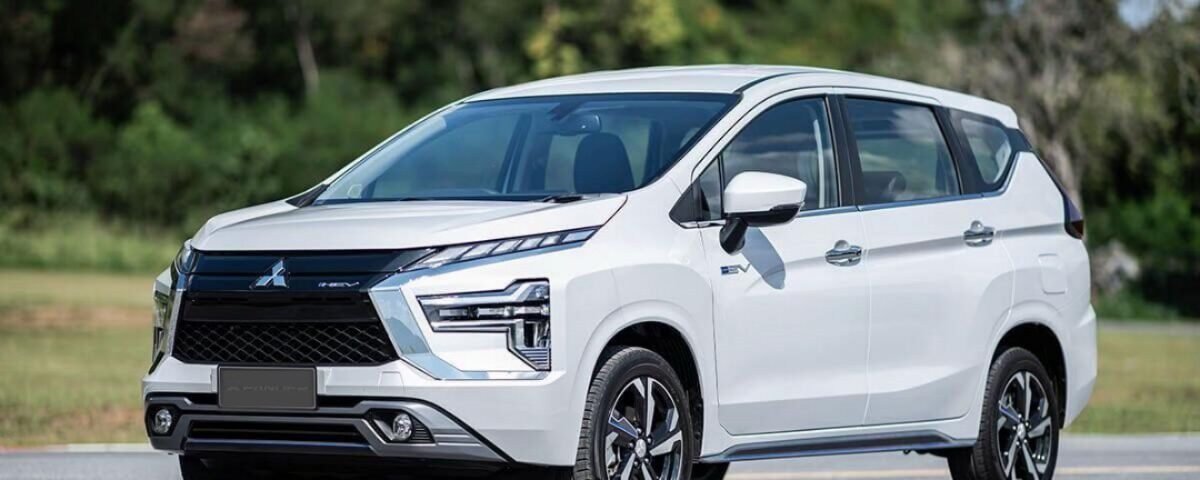 White Mitsubishi SUV shown in a three-quarter front view on a sunny roadway with trees in the background.