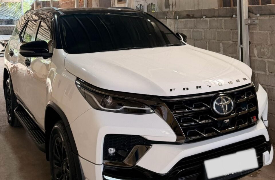 White Toyota Fortuner SUV parked in a covered garage beside a brick wall, front three-quarter view with tinted windows and black trim.