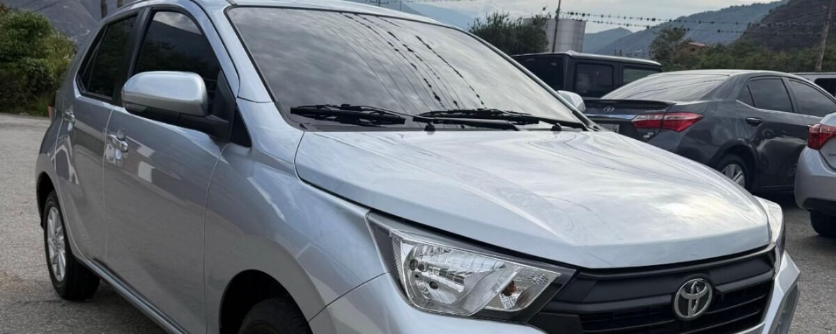 Silver Toyota sedan parked in a lot, front-left angle with mountains in the background and power lines overhead.