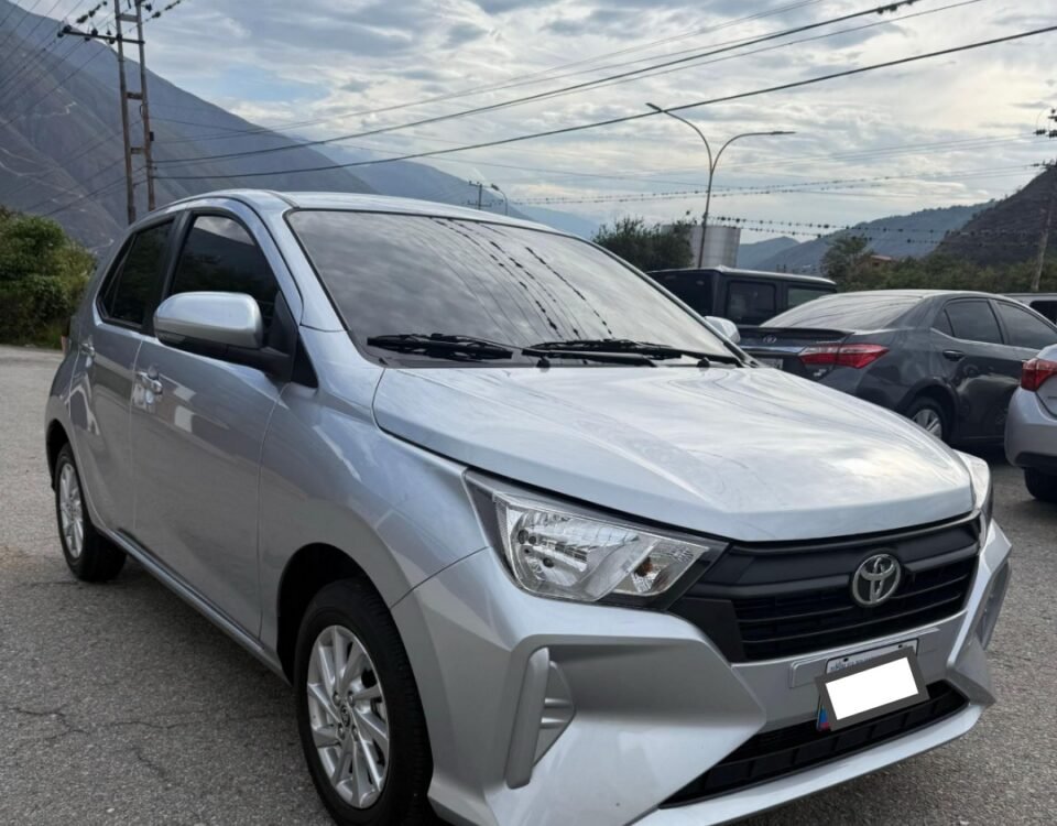 Silver Toyota sedan parked in a lot, front-left angle with mountains in the background and power lines overhead.