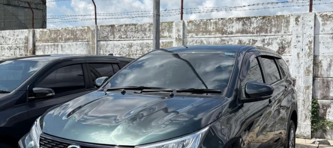 Dark gray SUV parked in a lot beside a weathered concrete wall with barbed wire, under a blue sky with fluffy clouds.