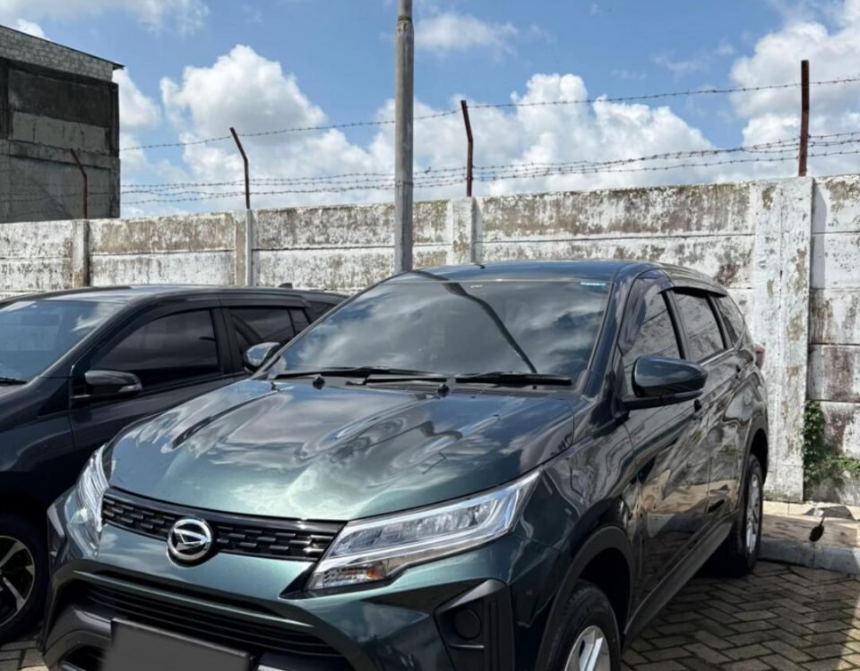 Dark gray SUV parked in a lot beside a weathered concrete wall with barbed wire, under a blue sky with fluffy clouds.